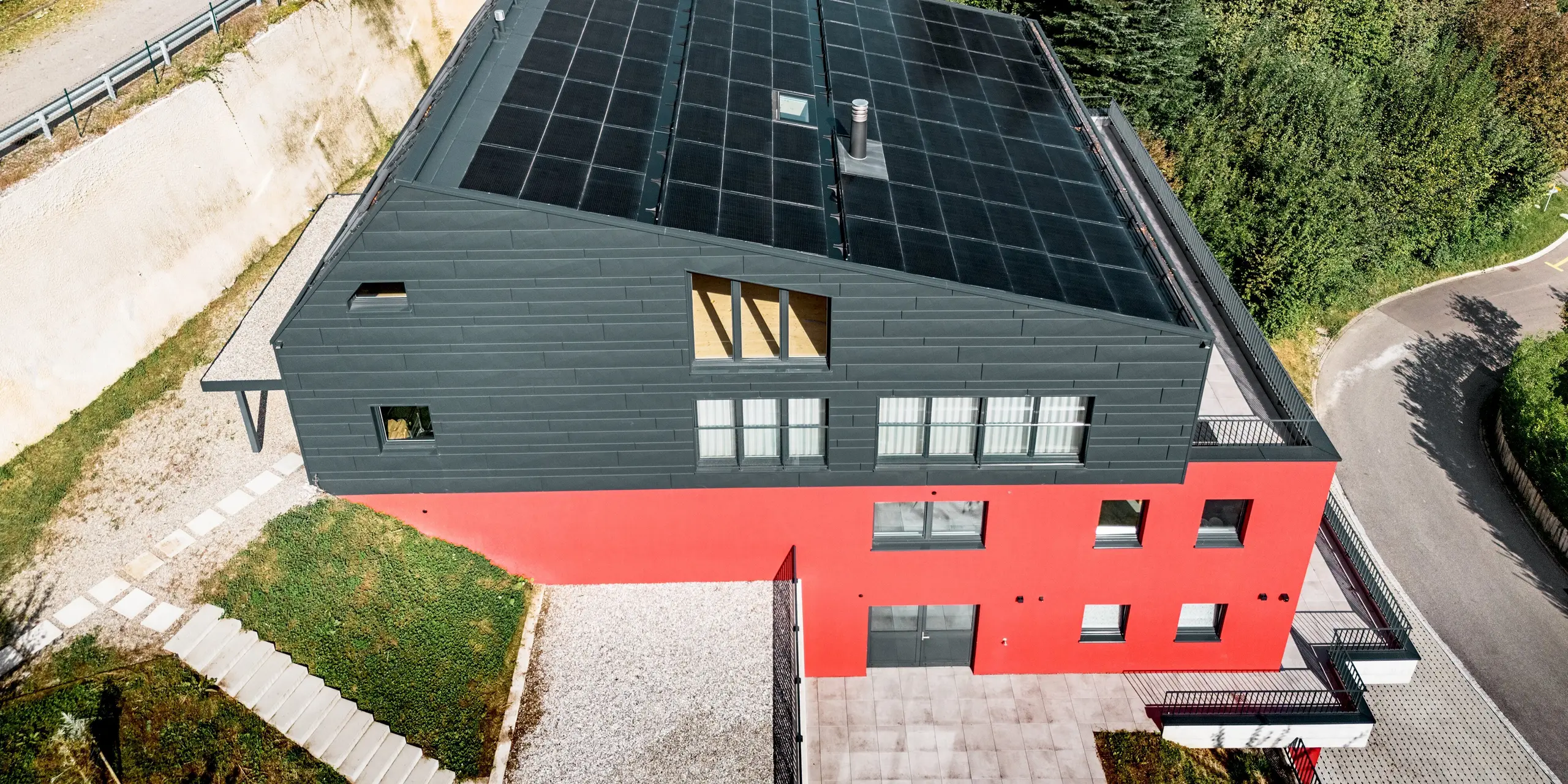Aus der Vogelperspektive zeigt sich das Weinwerk in Wienacht-Tobel eindrucksvoll inmitten der Hügellandschaft über dem Bodensee. Das PREFA Dachpaneel FX.12 und die Siding.X-Fassade in der Farbe P.10 Anthrazit verleihen dem Gebäude eine markante, monolithische Optik. Die langlebigen Aluminiumprodukte bilden einen starken Kontrast zur roten Farbe der unteren Geschosse.