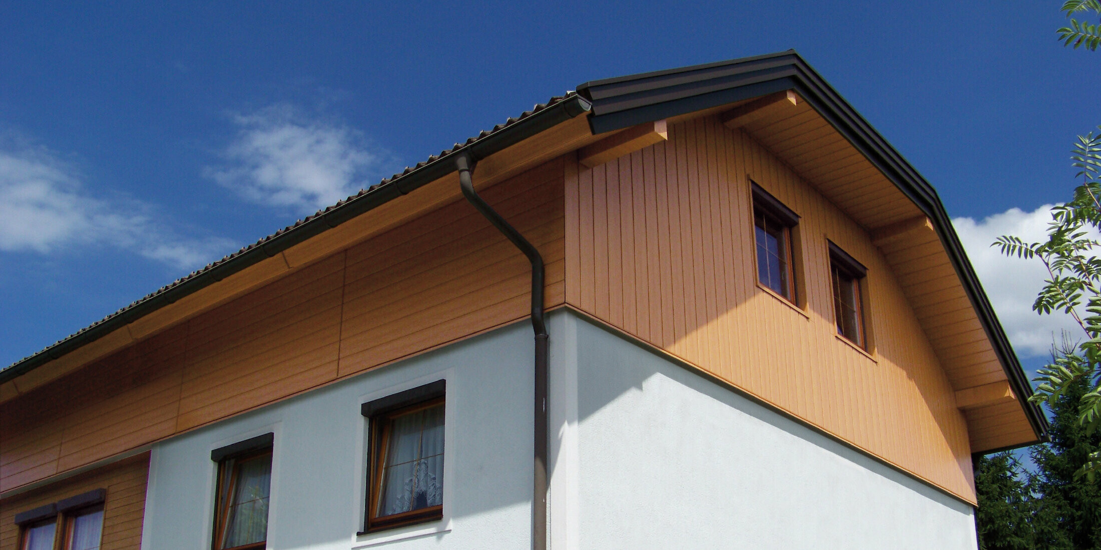 Casa unifamiliare di grandi dimensioni con tetto a due spioventi con falda a timpano e rivestimento del timpano con doghe di rivestimento PREFA con effetto legno chiaro