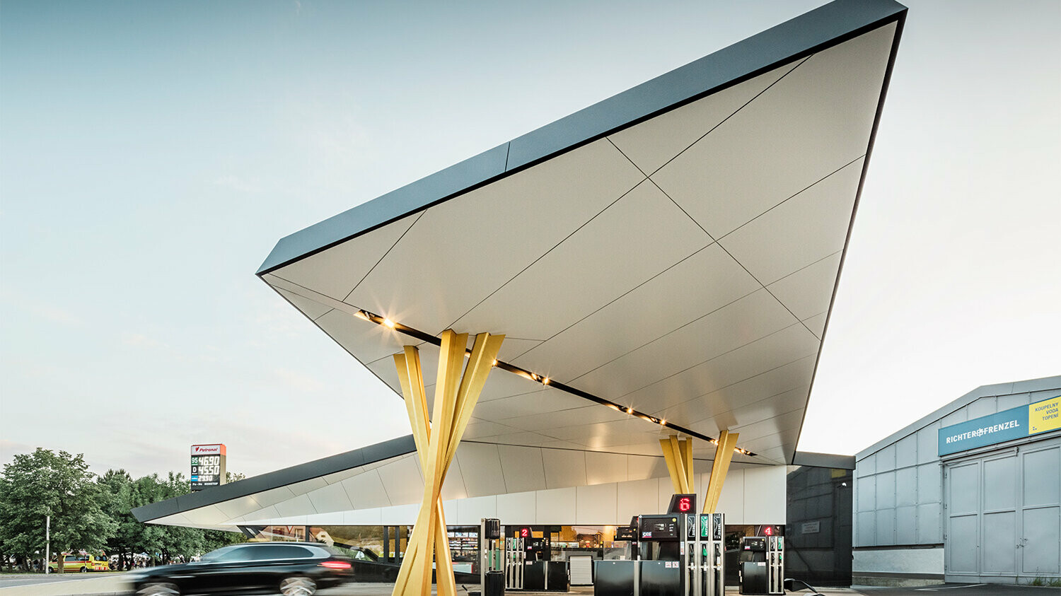 Seitliche Ansicht der Tankstelle mit einer Untersicht des Daches, welches auf zwei goldenen Stützengruppen aufliegt.