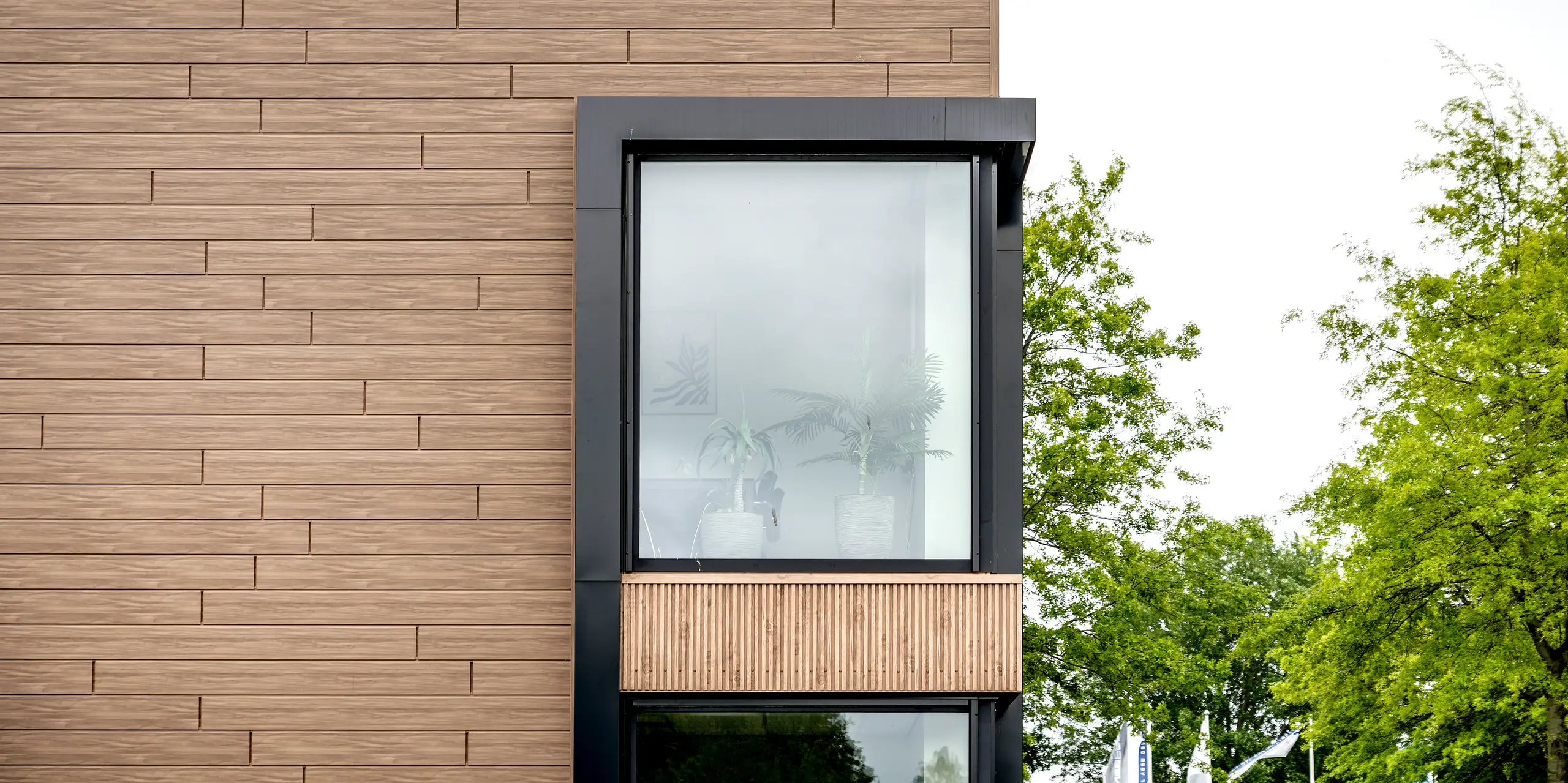 Die moderne Gebäudefassade der Dokter Schoonmaakorganisatie in Wolvega beeindruckt mit einer klaren Formensprache und einer harmonischen Verbindung aus Architektur und Natur. Großzügige, schwarz gerahmte Fenster setzen markante Akzente in der walnussbraunen PREFA Fassade. Die PREFA Sidings in Holzoptik verleihen dem Bauwerk eine warme Ausstrahlung und bieten zugleich die langlebigen, witterungsbeständigen Vorteile von Aluminium.