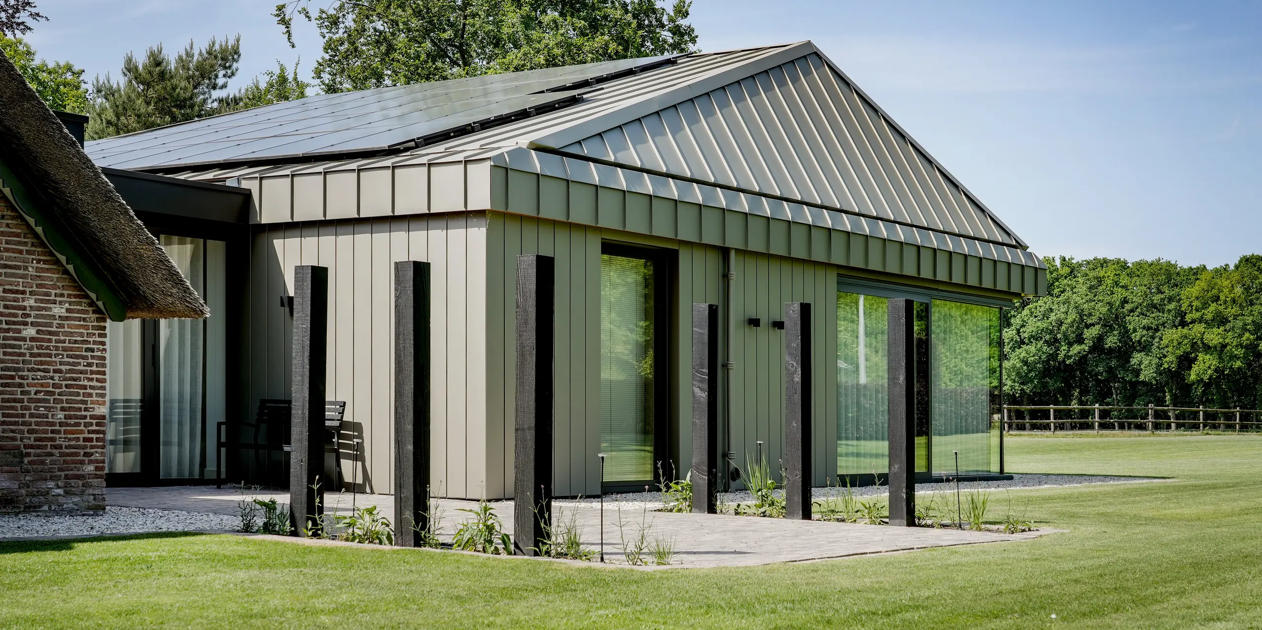 Der moderne Erweiterungsbau in Putten fasziniert mit einer nahtlosen Hülle aus PREFALZ Aluminium für Dach und Fassade. Großzügige Glasflächen und markante Winkelstehfalze setzen starke architektonische Akzente. Im spannenden Dialog mit dem traditionellen Reetdach überzeugt das langlebige PREFA Aluminium durch hochwertige Optik, Nachhaltigkeit und Witterungsbeständigkeit.