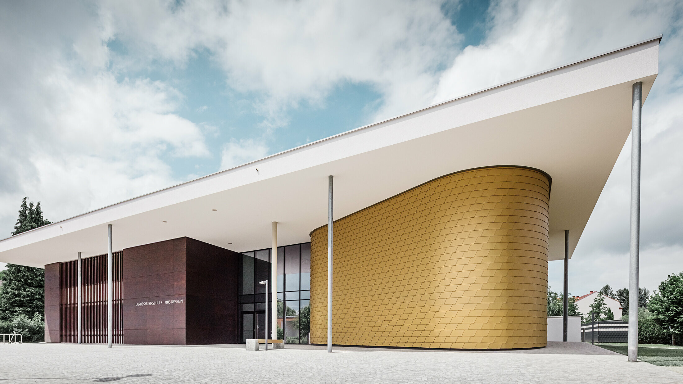 Goldene Aluminiumschindeln von PREFA schmücken die gerundete Fassade der Musikschule