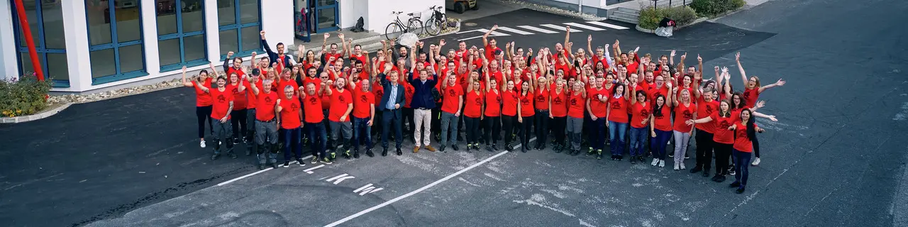 PREFA MitarbeiterInnen mit rotem PREFA T-Shirt stehen in einem Halbkreis vor dem Bürogebäude in Marktl.