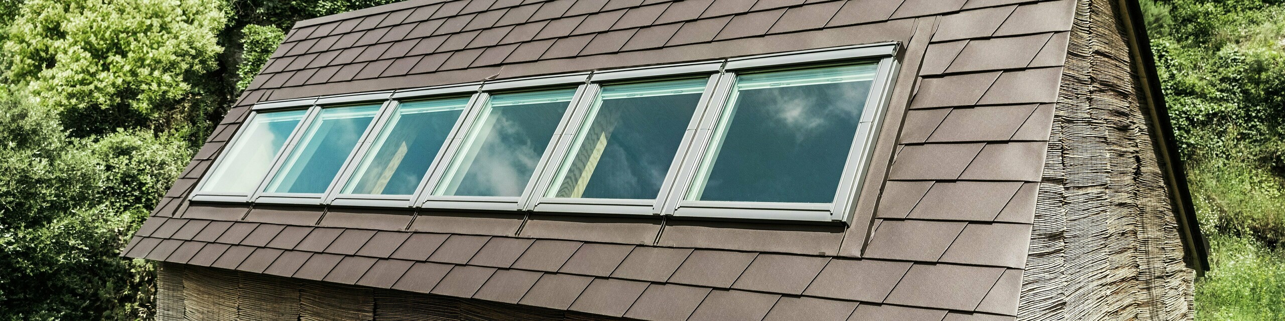 Scandole PREFA in P.10 testa di moro su un tetto di una casa moderna con lucernari - soluzione per tetti in alluminio durevole per un design di copertura efficiente dal punto di vista energetico ed elegante.