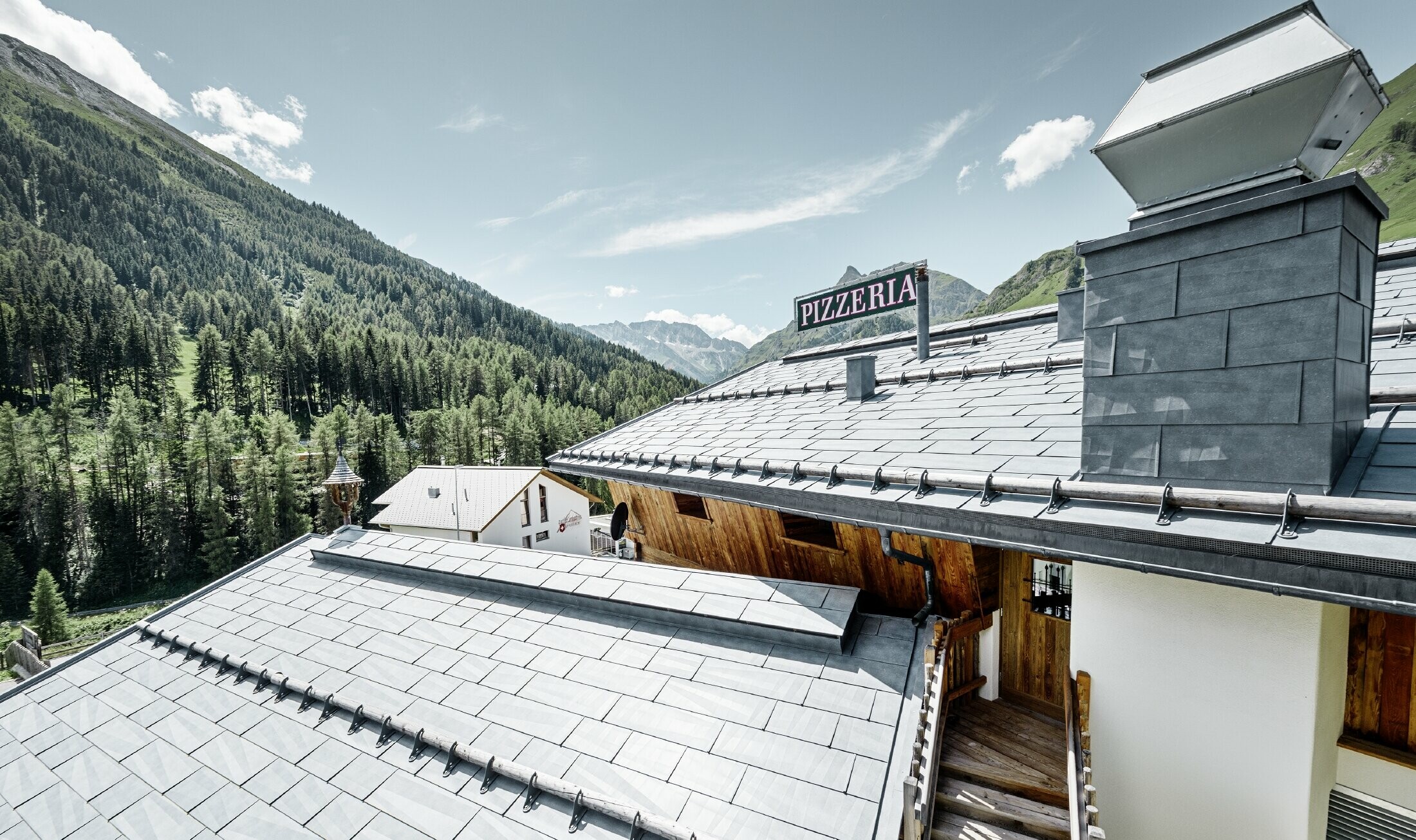 Ristorante Almrausch con montagne sullo sfondo e una copertura PREFA con il pannello per coperture FX.12 in grigio pietra e fermaneve