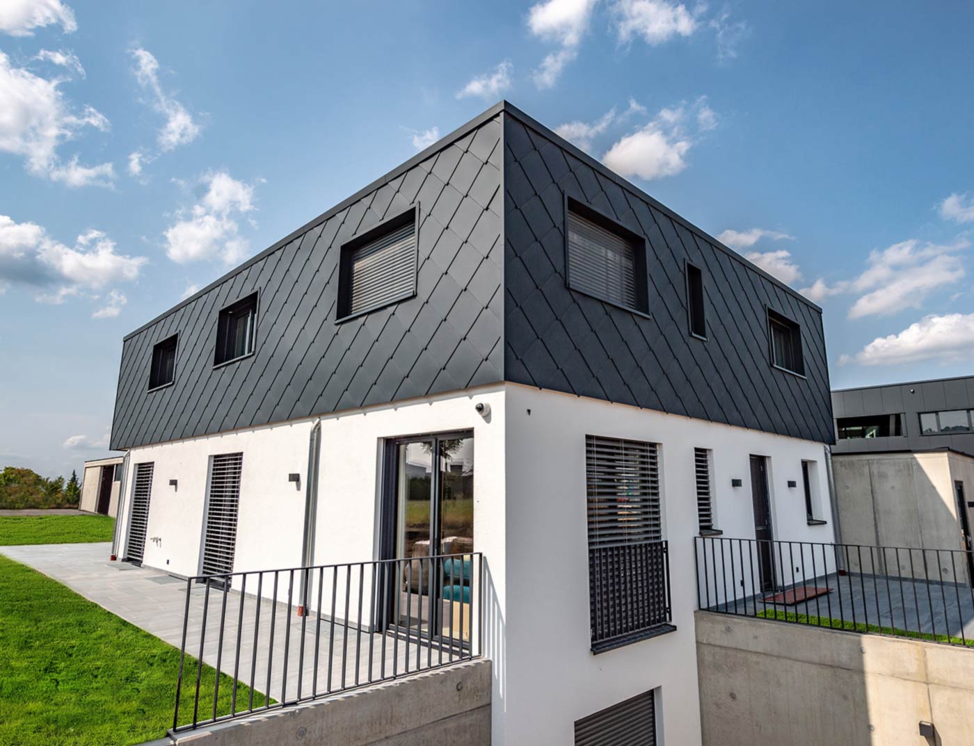 Losanga 44 x 44 PREFA, referenza antracite Nuova costruzione moderna con copertura piatta - la facciata del piano superiore è rivestita di losanghe in alluminio 44 x 44 PREFA di colore antracite. La parte inferiore della facciata è intonacata di bianco.